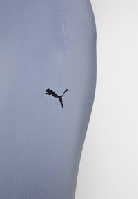 Jasnoniebieskie legginsy sportowe wykonane z elastycznego materiału, z czarnym logo Pumy i widocznymi detalami przeszycia.