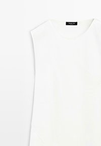 Witte mouwloze top met ronde hals en schoudervullingen, plat gelegd, label "Massimo Dutti" zichtbaar aan de binnenkant van de hals.