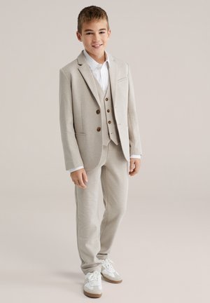 Béžový oblek s dvouknoflíkovým sakem a třídílnou vestičkou, doplněný bílou košilí a světle šedými kalhotami. Bílé tenisky s hnědými detaily.