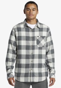 Camicia di flanella a quadri grigia e bianca con maniche lunghe, chiusura a bottoni davanti e una tasca sul petto, realizzata in tessuto testurizzato.