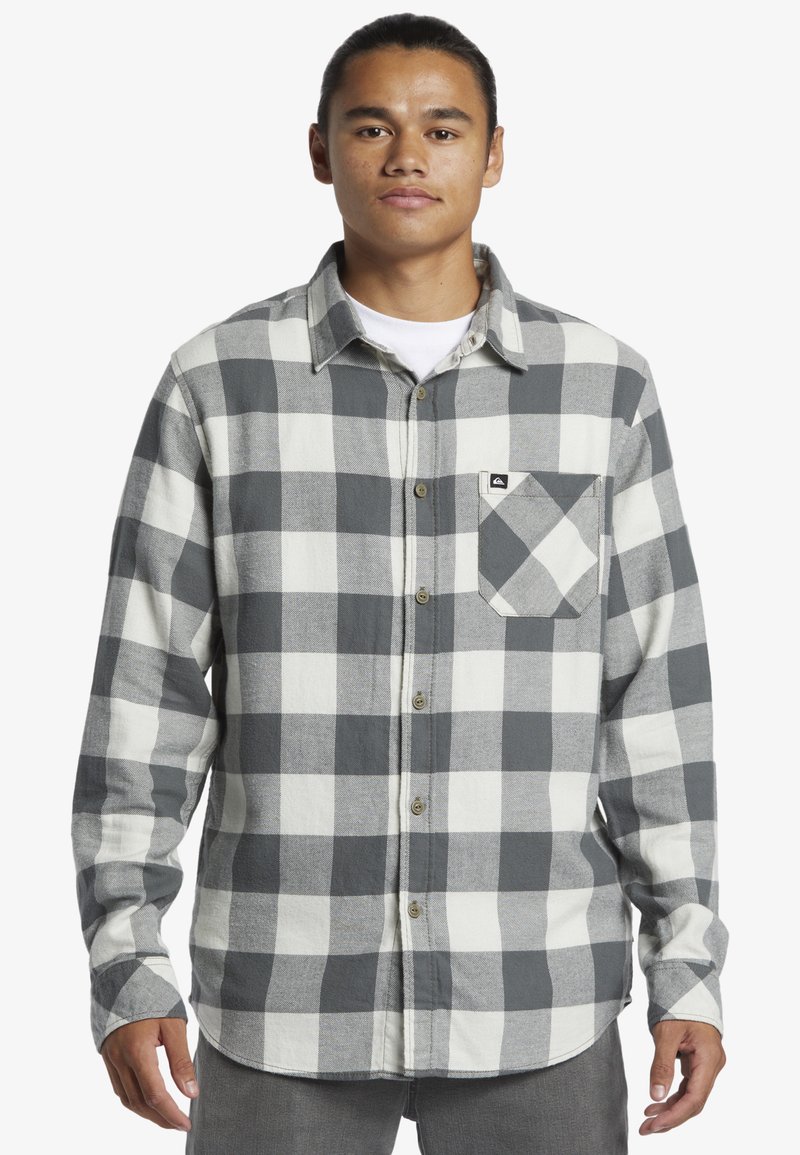 Camicia di flanella a quadri grigia e bianca con maniche lunghe, chiusura a bottoni davanti e una tasca sul petto, realizzata in tessuto testurizzato.