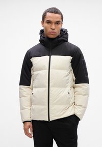 Puffjakke i creme- og sort farveblokdesign, med lynlås foran, hætte og quiltede sektioner. Glat tekstur med et moderne fit.