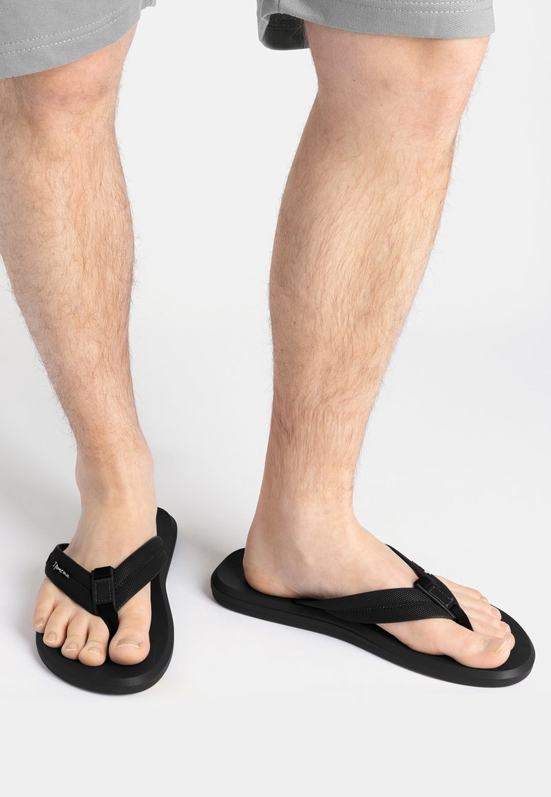 Schwarze Flip-Flops mit flacher Sohle, weichen Riemen und Zehensteg. Die Riemen haben eine strukturierte Oberfläche für besseren Halt.