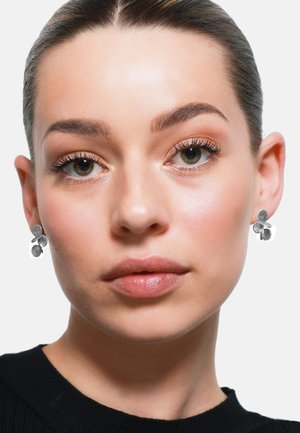 Pendientes florales de plata con pétalos texturizados, presentando un diseño de tres pétalos. La piel del modelo tiene una complexión suave y natural.