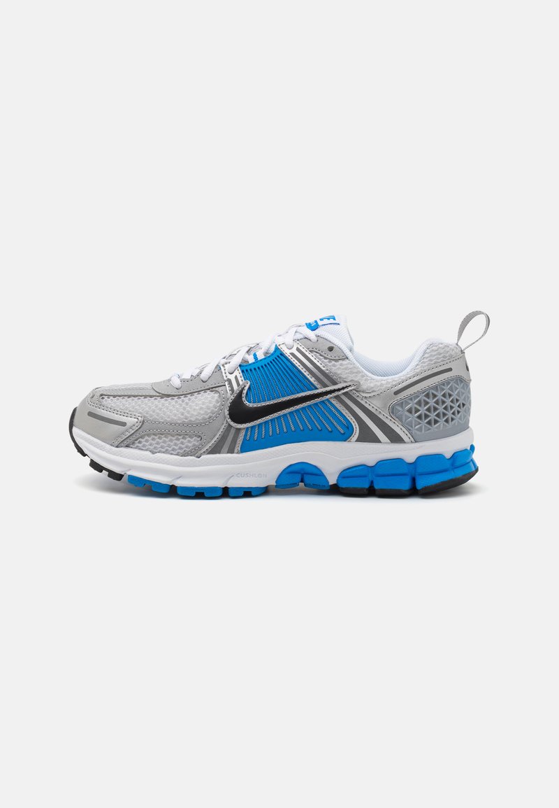 Chaussure de sport grise avec des accents bleus, composée de matériaux en maille et synthétiques, au design incurvé, avec une semelle rembourrée et un talon texturé.