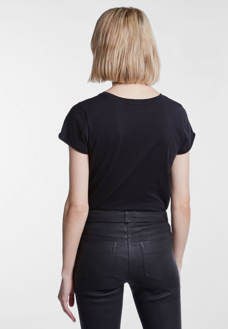 Camisa negra de manga corta hecha de tela suave, vista desde la parte de atrás, combinada con pantalones de cuero negro de tiro alto con bolsillos traseros.
