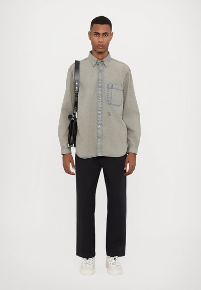 Ljusgrå denimskjorta med knäppning, en bröstficka och kontrasterande blå sömmar, tillsammans med svarta byxor och vita sneakers.
