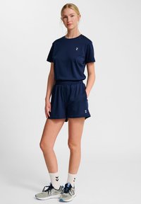 Marinblått träningsset som består av en t-shirt med kort ärm och shorts med elastisk midja. Inkluderar vita logotypdetaljer, parat med ljusa sneakers och strumpor.