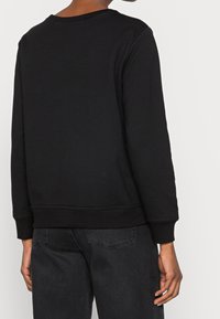 Svart sweatshirt med rund halsringning, ribbade ärmslut och nederkant. Mjukt tyg, enkel design. Kombinerad med mörka jeans.