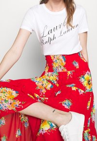 Weißes T-Shirt mit schwarzem, kursivem Text, kombiniert mit einem leuchtend roten Rock mit mehrfarbigen Blumenmustern und einem elastischen Bund.