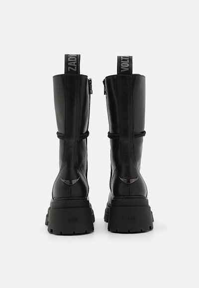 Black leather ankle boots with a chunky sole, side zippers, and logo-embossed pull tabs. Features decorative stitching and wing accents.