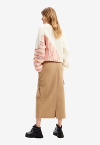 Strikkegenser med rosa og hvit mønster, cargo skjørt i beige og svarte snørestøvler, som viser ribbet tekstur og vid passform.