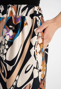Spódnica w wzory z abstrakcyjnymi motywami w kolorach czarnym, beżowym i brązowym, z detalem w postaci kieszeni. Wykonana z gładkiego, lekkiego materiału z elastycznym pasem.