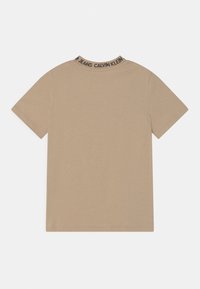 T-shirt beige à manches courtes en coton avec un bandeau logo noir autour du col. Design simple avec une coupe décontractée et des coutures minimales.