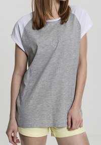 Camiseta gris de manga corta con mangas raglán blancas, hecha de un tejido suave. Presenta un corte relajado y un escote redondeado, combinada con pantalones cortos amarillos.