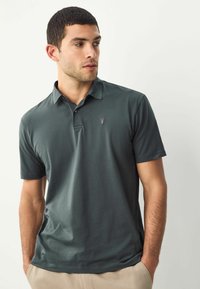 Donkergroen polo met korte mouwen, een puntige kraag en een klein geborduurd logo. Gemaakt van een gladde, lichte stof.