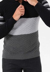 Knitted zip-up sweater featuring horizontal stripes in black, gray, and light gray. Textured pattern with ribbed cuffs and hem.