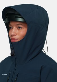 Navy hooded jacket with a high collar, front zipper, and adjustable drawstring hood; features two zippered chest pockets and smooth texture.