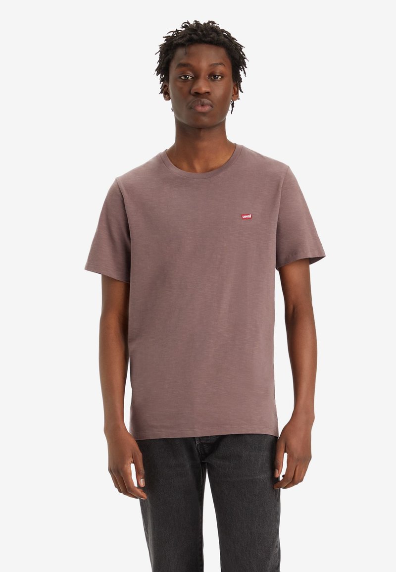 Braunes Baumwoll-T-Shirt mit kurzen Ärmeln und Rundhalsausschnitt, mit einem kleinen roten "Levi's"-Logo auf der Brust. Getragen mit dunklen Jeans.