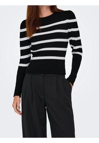 Pull en maille côtelée rayé noir et blanc à manches longues, associé à un pantalon noir à rayures fines taille haute ; coupe ajustée, matériau texturé.