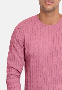 Jersey de punto en color rosa claro. Cuello redondo, mangas largas, patrón texturizado, hilo grueso y puños acanalados. Ejemplo de diseño de prendas de punto.