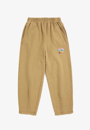 Pantalon de survêtement en polaire beige avec taille élastique, poches latérales et un petit patch coloré sur la partie supérieure de la jambe droite.