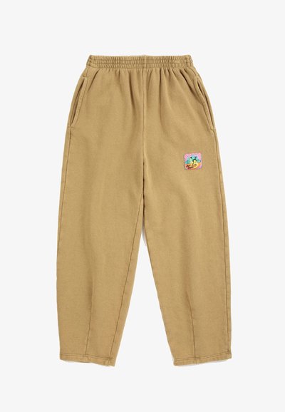 Pantalon de survêtement en polaire beige avec taille élastique, poches latérales et un petit patch coloré sur la partie supérieure de la jambe droite.