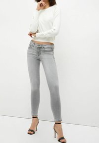 Biały sweter dziany z fakturowanymi rękawami, zestawiony z jasnoszarymi obcisłymi jeansami z delikatnym wyblaknięciem i ozdobnym łańcuszkiem przy nogawkach. Czarne szpilki.