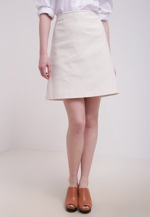 Hvid tekstureret A-formet nederdel med en glat finish, kombineret med brune mule-sandaler med åbne tæer. Har en figursyet talje og en udvidet kant.