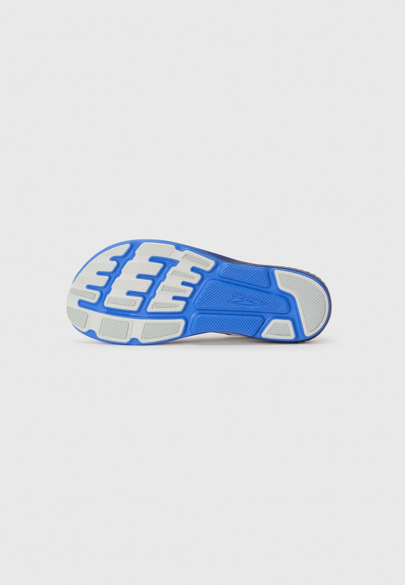 Suela de zapato deportivo con una superficie de goma blanca texturizada y acentos azules, diseñada para ofrecer tracción, con surcos y patrones distintivos.