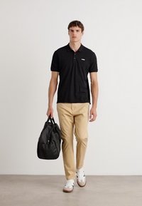 Zwarte polo, beige broek, met een zwarte tas. Witte sneakers met bruine zolen. Eenvoudig, functioneel ontwerp met minimale accenten.