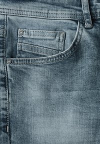 Jeans de denim azul claro con un bolsillo frontal que presenta un botón a presión plateado, costuras visibles y un acabado suave y texturizado.