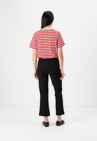 Red and white striped short-sleeve shirt with a round neckline, paired with black flared pants, shown from the back. Black footwear visible.