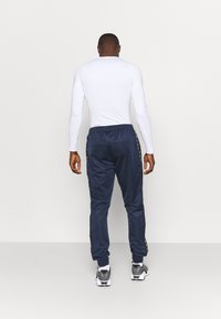 Top blanco de manga larga combinado con pantalones deportivos azul oscuro que presentan franjas laterales. Los pantalones tienen un corte ajustado y puños elásticos.