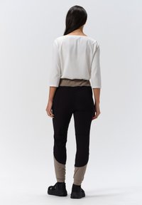 Women’s outfit featuring a white top with 3/4 sleeves and black multifunctional pants with beige accents and fitted cuffs.