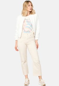 Bela teksturirana bomber jakna preko svetlega grafičnega T-majice s pastelnimi vrtinčastimi motivi. Paired s svetlimi skrajšanimi hlačami in svetlimi teniskami.