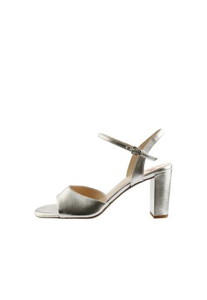 Zilveren damessandaal met open teen, blokhak en verstelbare enkelriem met gesp, op een witte achtergrond.