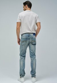 Vaqueros de denim azul claro con corte ajustado, que cuentan con bolsillos traseros y un parche de marca. Combinados con una camiseta blanca de manga corta y zapatillas blancas.