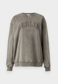 Felpa grigia in cotone con collo rotondo, spalle abbassate e polsini a costine. Presenta la scritta "BERLIN" in grandi lettere scure e una leggera texture.