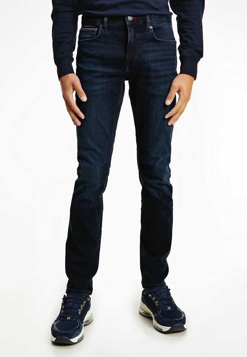 Vaqueros azul oscuro de corte slim, con cinco bolsillos, cremallera en la bragueta y costuras en contraste, combinados con zapatillas oscuras.