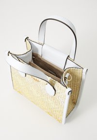Geweven rieten handtas met witte leren accenten. Bevat twee handvatten bovenaan en een lichtbeige interieur met een ritszak. Open ontwerp.