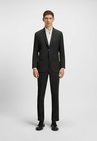 Black pinstriped suit with a slim fit, single-button jacket, notch lapels, and matching trousers. Paired with a white dress shirt and black shoes.