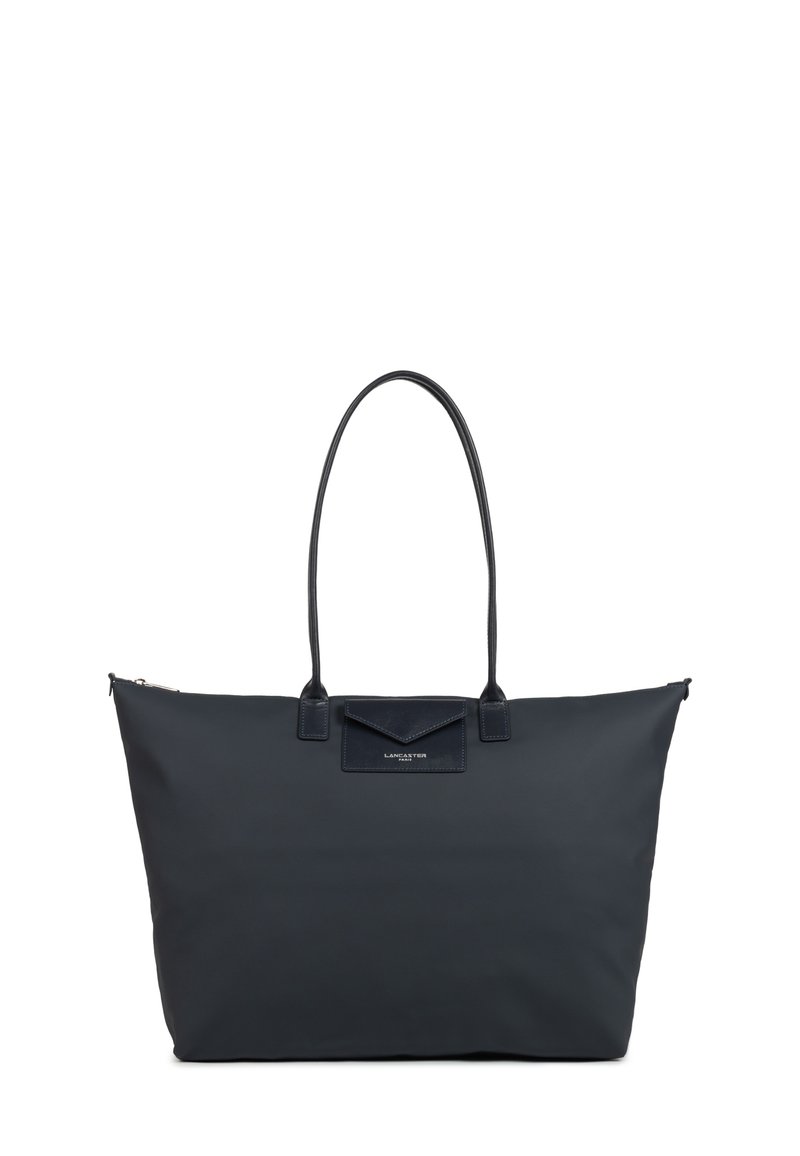 Grande borsa tote nera in tessuto morbido, con due manici in pelle e una tasca a patta. Presenta una chiusura con zip e un dettaglio del logo sulla parte anteriore.