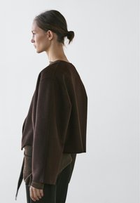 Brown oversized sweater with a wide neckline and dropped shoulders, featuring a textured layer at the bottom. Smooth fabric against skin.