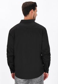 Maglietta nera a maniche lunghe con colletto a punta, texture liscia e polsini con bottoni; presenta un design a yoke nella parte posteriore.