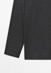 Mørkegrå langærmet beklædningsgenstand foldet med synlig sidesøm og kant mod en hvid baggrund.