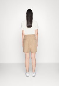 Pantaloni corti beige con cintura elastica, dotati di due tasche posteriori. Abbinati a una maglietta chiara e a sneakers bianche.