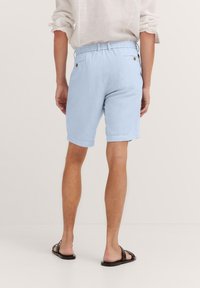 Light blue linen shorts with an elastic waistband, side pockets, and a back pocket, paired with black sandals. Defined hem and relaxed fit.