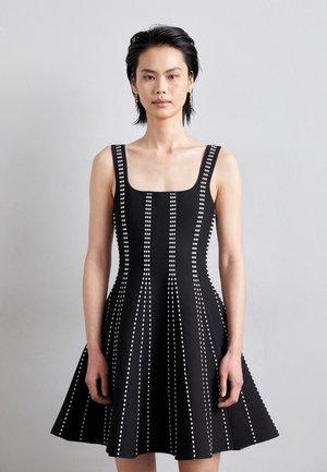 Zwarte jurk met een aansluitende bodice en een flared rok, met witte verticale strepen en een vierkante halslijn. De stof heeft een gladde textuur.