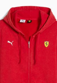 Rød zip-up hættetrøje lavet af blødt stof med et hvidt Puma-logo og et gult Ferrari-emblem, udstyret med snøre i hætten.